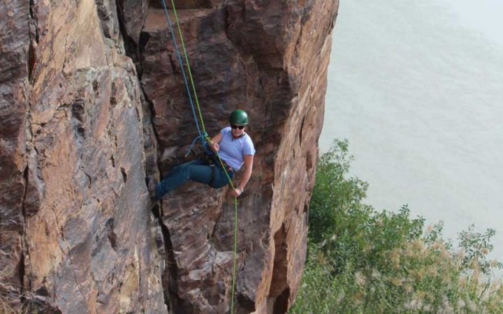a person rappels down a rock walk in texas. there is a body of water below them.